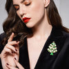 Woman wearing a green Christmas tree brooch on a black blazer against a gray background