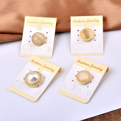 Four pairs of gold and pearl magnetic brooches on jewelry cards against a brown fabric background.