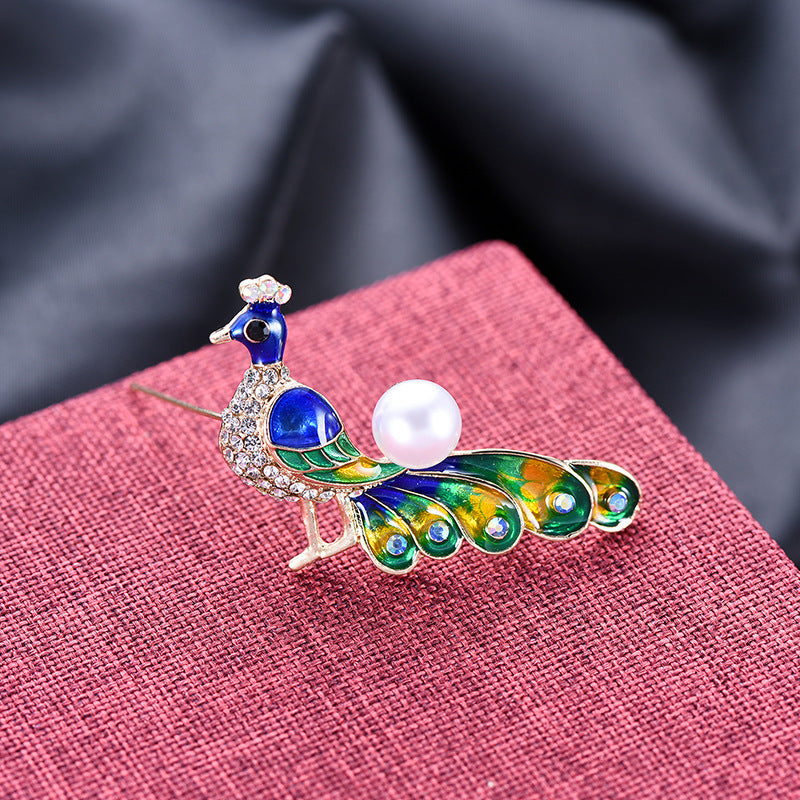 Peacock-shaped brooch with a pearl on a pink fabric background