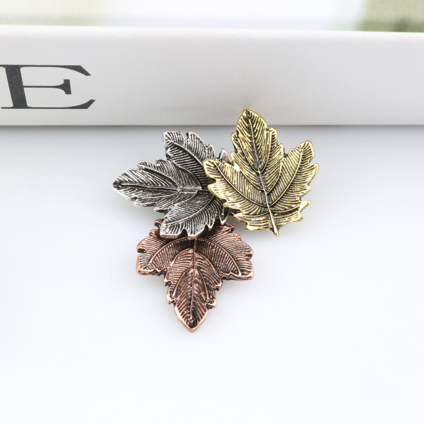 Three leaf-shaped pins in gold, silver, and bronze on a white surface.