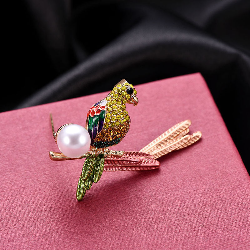 Decorative parrot brooch with a pearl on a pink surface