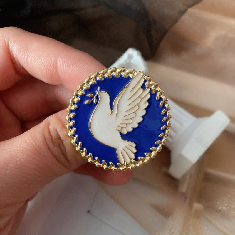Pin with a dove design held by a hand against a blurred background
