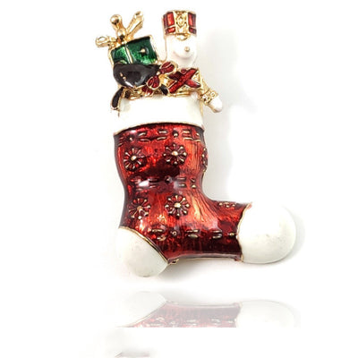 Decorative brooch in the shape of a red boot with a small figure on top, on a white background.