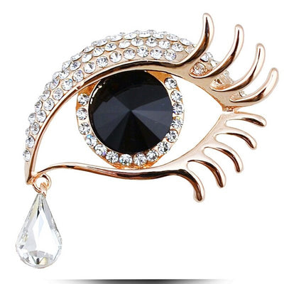 Decorative brooch shaped like an eye with crystals and a teardrop on a white background