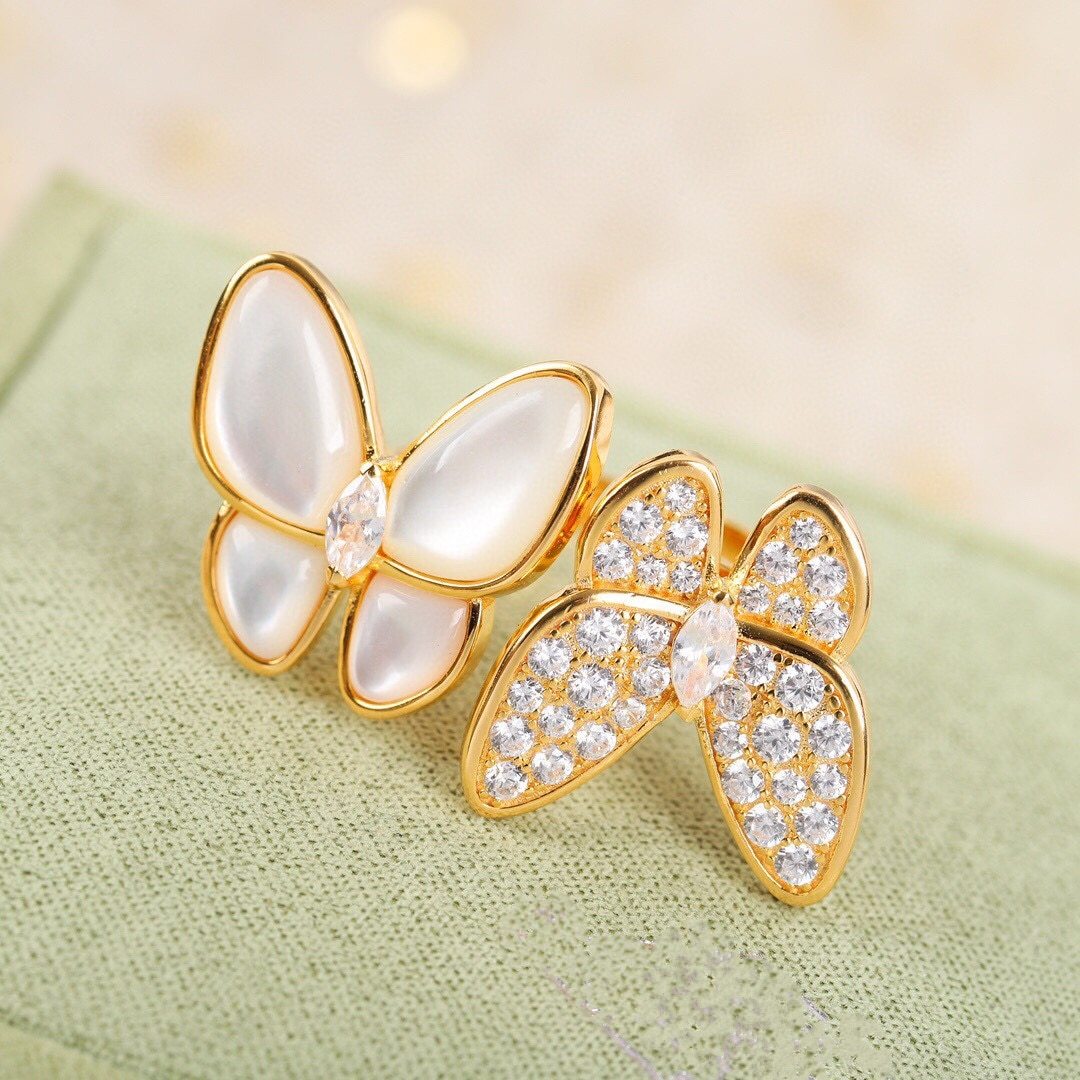 Butterfly-shaped earrings with gold and crystal details on a light green fabric background