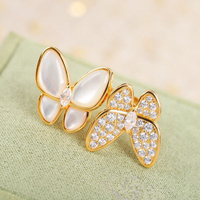 Butterfly-shaped earrings with gold and crystal details on a light green fabric background