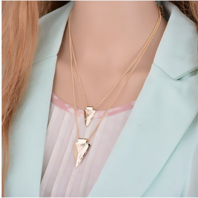 Gold triangle pendant necklace on a mannequin with a light blue jacket and pink top.