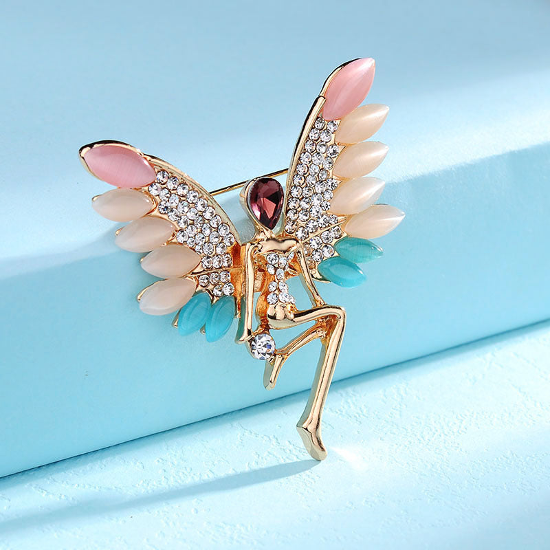 Decorative brooch with angel wings and pink gemstones on a light blue background