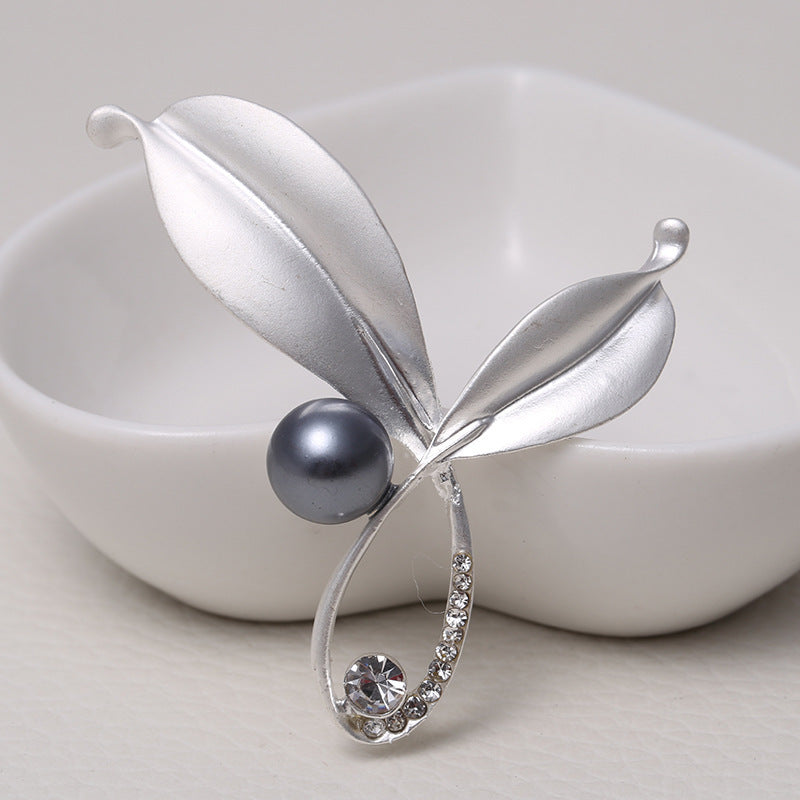 Silver brooch with a pearl and gemstone on a white background
