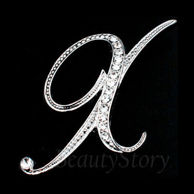 Silver brooch with a decorative letter 'x' design on a black background, branded 'BeautyStory'.