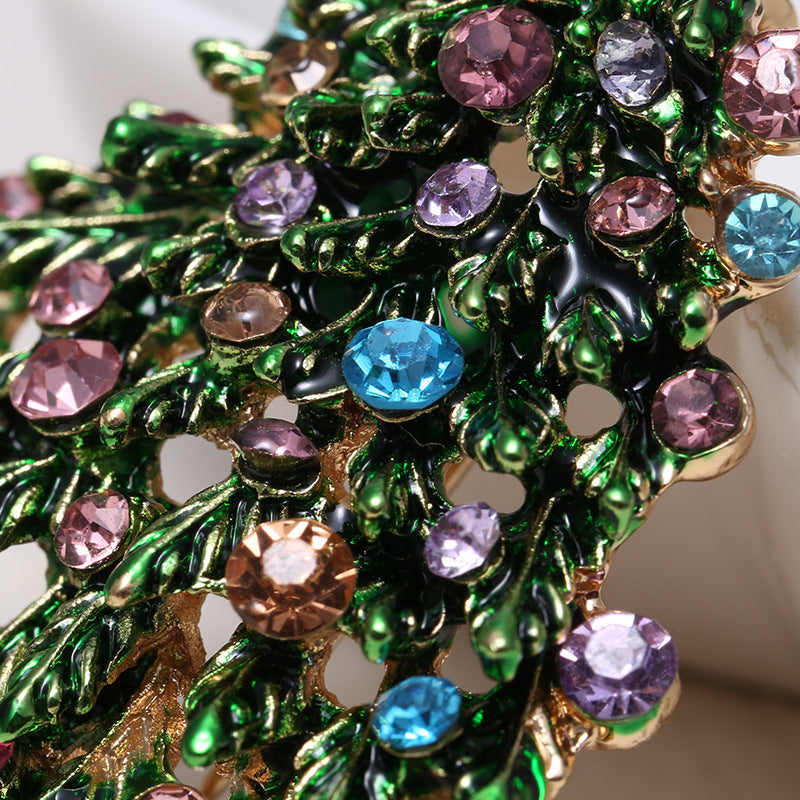 Close-up of a decorative brooch with green leaves and multicolored gemstones.
