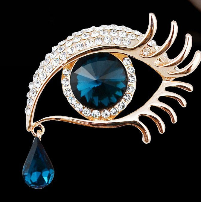 Jewelry eye-shaped brooch with blue gem and teardrop pendant on a black background