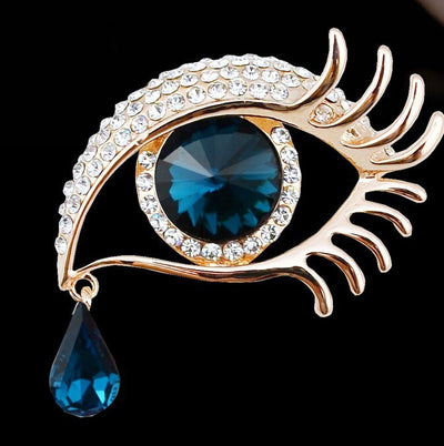 Jewelry eye-shaped brooch with blue gem and teardrop pendant on a black background