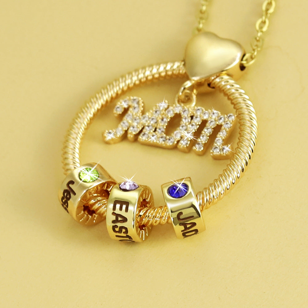 Gold necklace with 'MOM' pendant and three charms on a yellow background