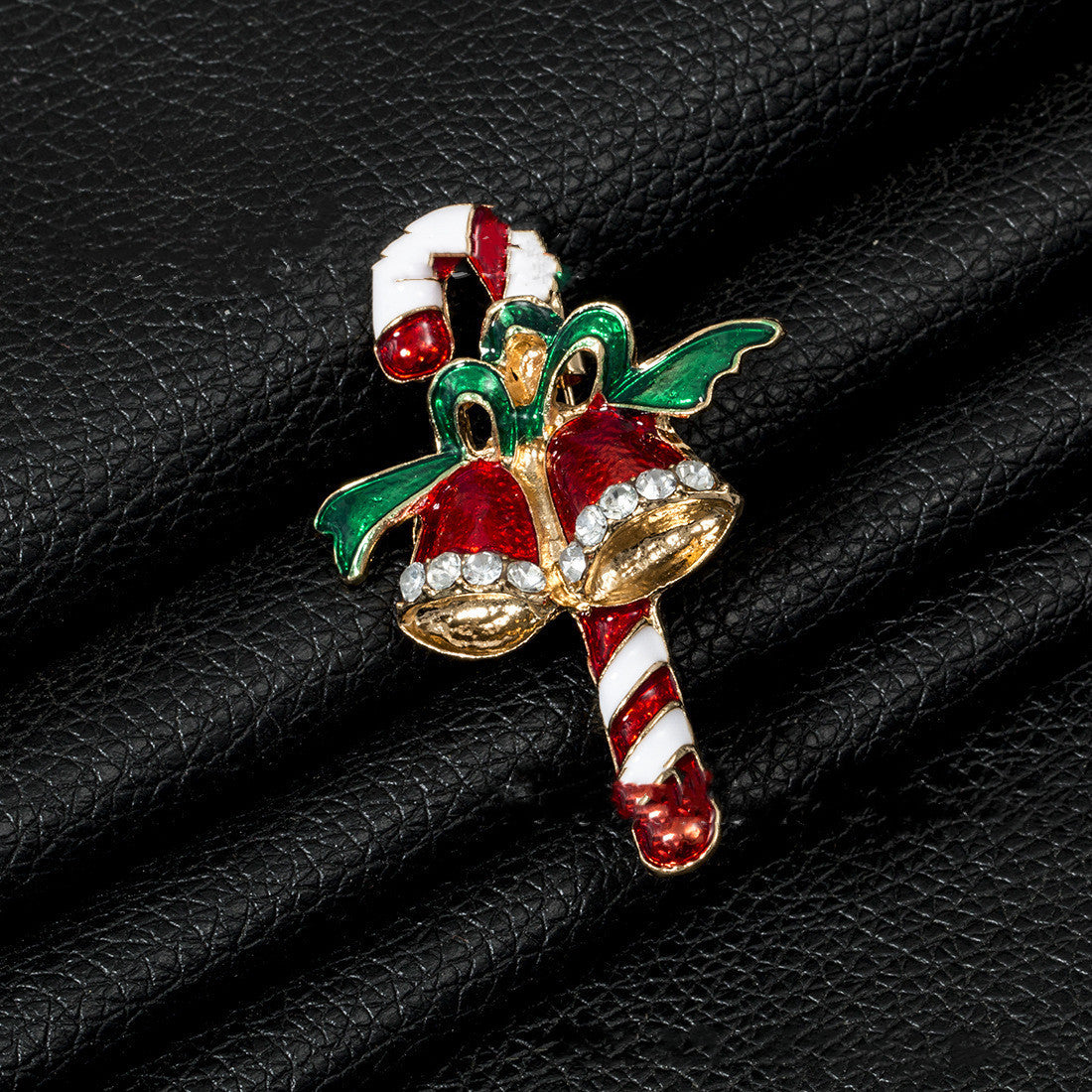 Christmas-themed brooch with candy cane and bell design on a black leather surface