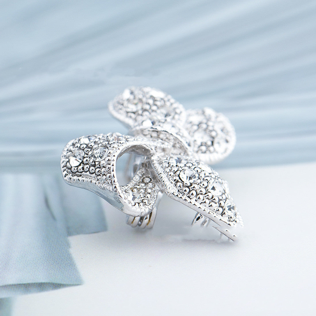 Silver leaf-shaped brooch with intricate detailing on a light blue fabric background