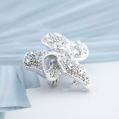 Silver leaf-shaped brooch with intricate detailing on a light blue fabric background