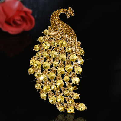 Gold peacock-shaped brooch with red rose in the background