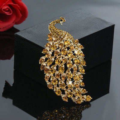 Gold peacock-shaped brooch with gemstones on a black box with a red rose in the background