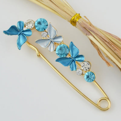 Decorative brooch with blue butterfly-shaped stones and gold accents on a white background