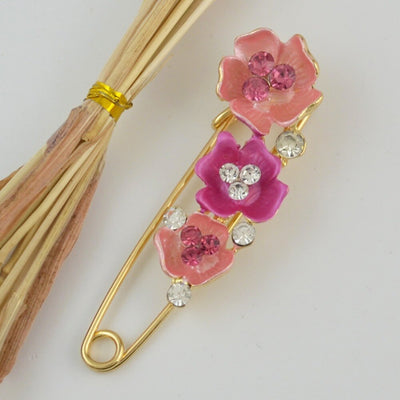 Decorative safety pin with pink flowers and crystals on a white background