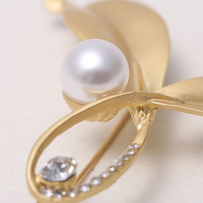 Gold bow-shaped brooch with a pearl and crystals on a light background
