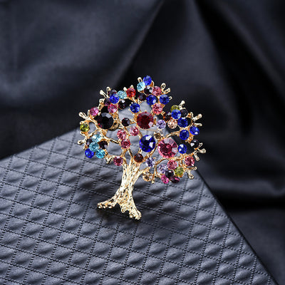 Decorative brooch shaped like a tree with colorful gemstones on a textured dark surface