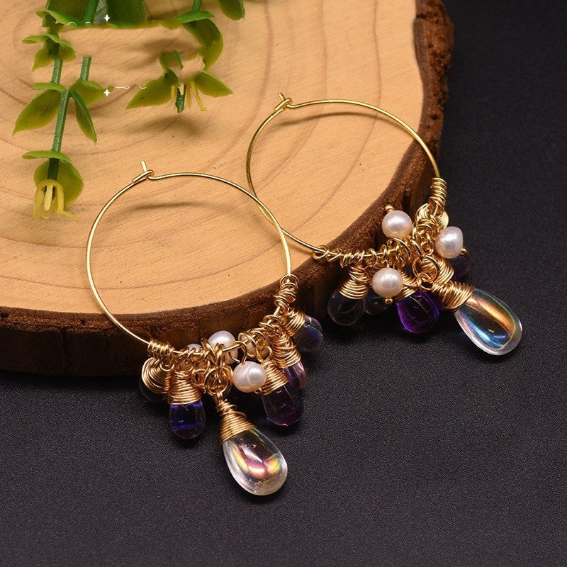 Gold hoop earrings adorned with purple and clear beads, accented by small white pearls, elegantly displayed on a wooden surface.