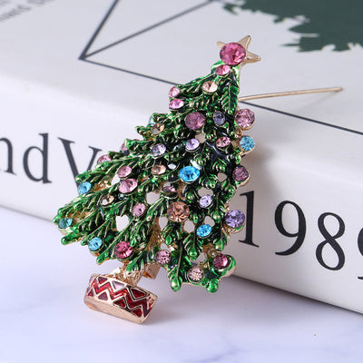 Decorative brooch shaped like a Christmas tree with colorful gemstones on a newspaper background.