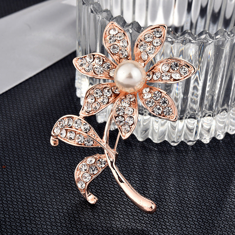 Rose gold flower brooch with pearl center on a dark textured surface