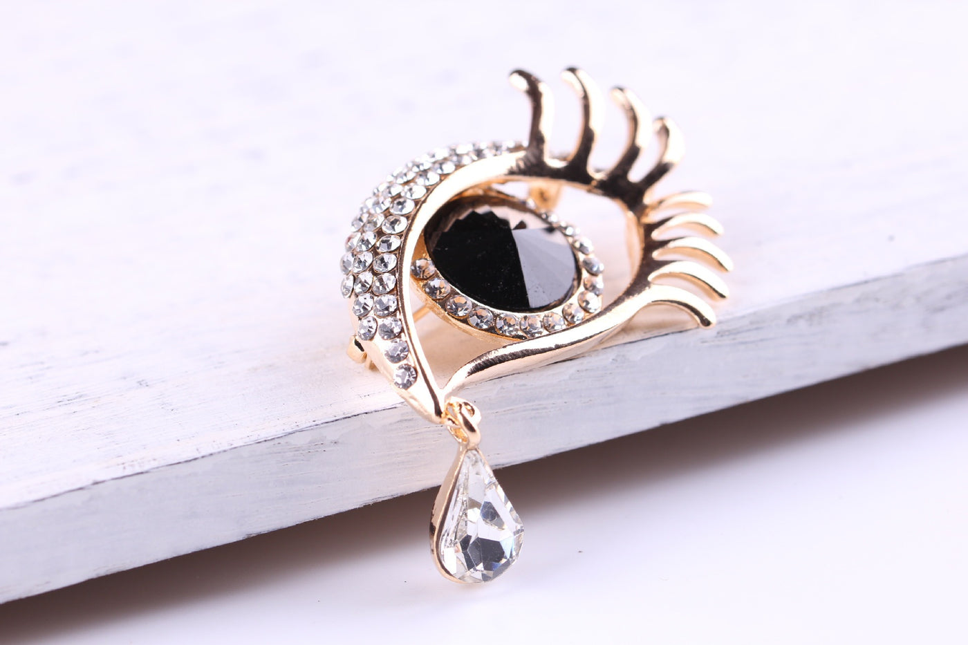 Decorative eye-shaped brooch with black gemstone and gold accents on a white surfaced 