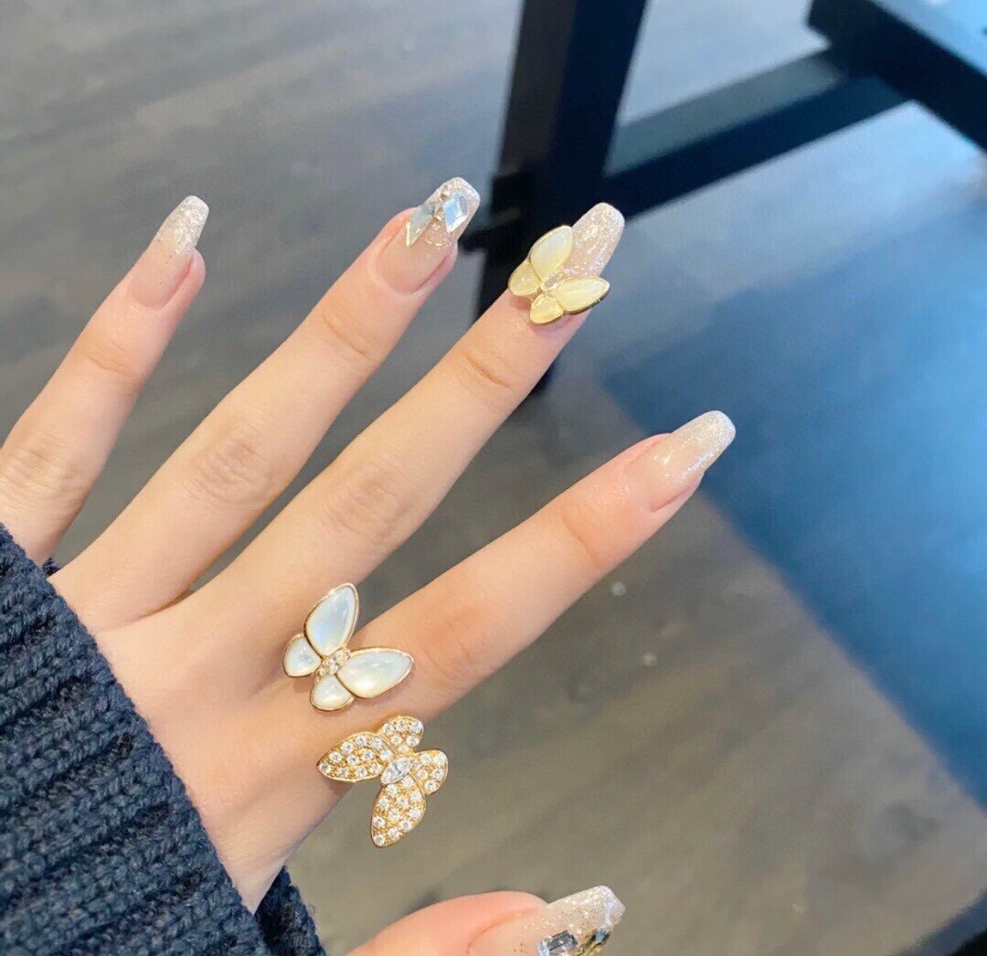 Hand with butterfly-shaped nail art and matching rings on a reflective surface