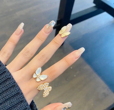 Hand with butterfly-shaped nail art and matching rings on a reflective surface