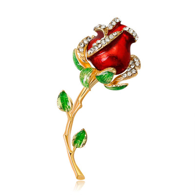 Red rose brooch with gold stem and green leaves on a white background