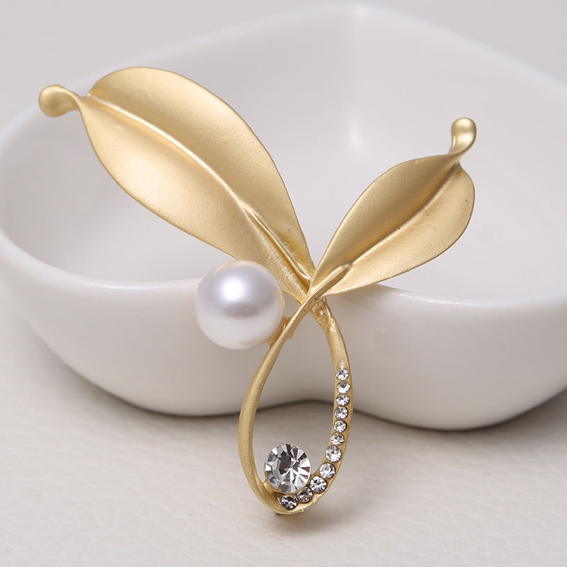 Gold leaf-shaped brooch with a pearl and crystal on a white background
