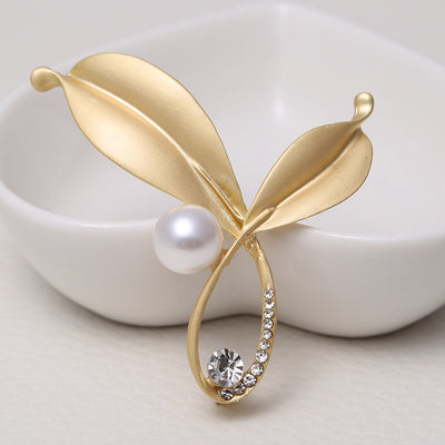Gold leaf-shaped brooch with a pearl and crystal on a white background