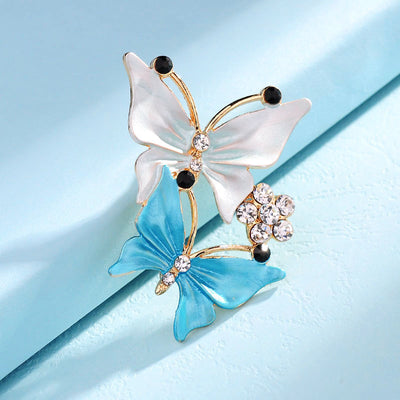 Butterfly-shaped brooch with white and blue wings on a light blue background