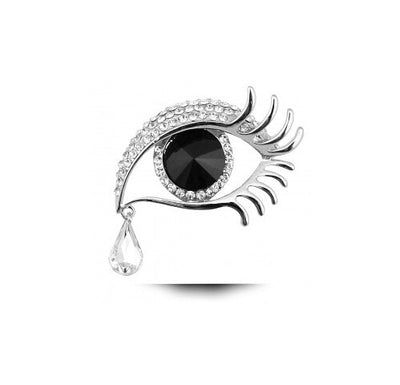 Jewelry piece resembling an eye with a black center and clear gemstones on a white background