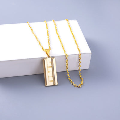 Gold necklace with a rectangular pendant on a light gray background