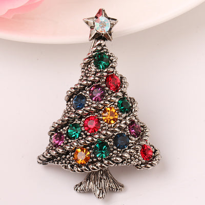 Silver Christmas tree-shaped brooch with colorful gemstones on a white background