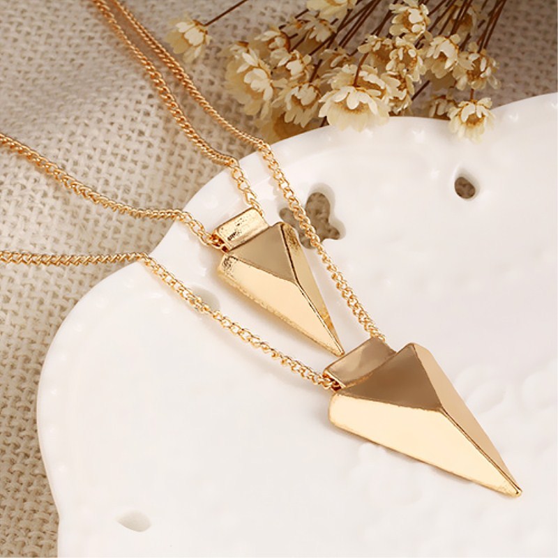 Gold necklace with geometric pendants on a white shell with dried flowers in the background