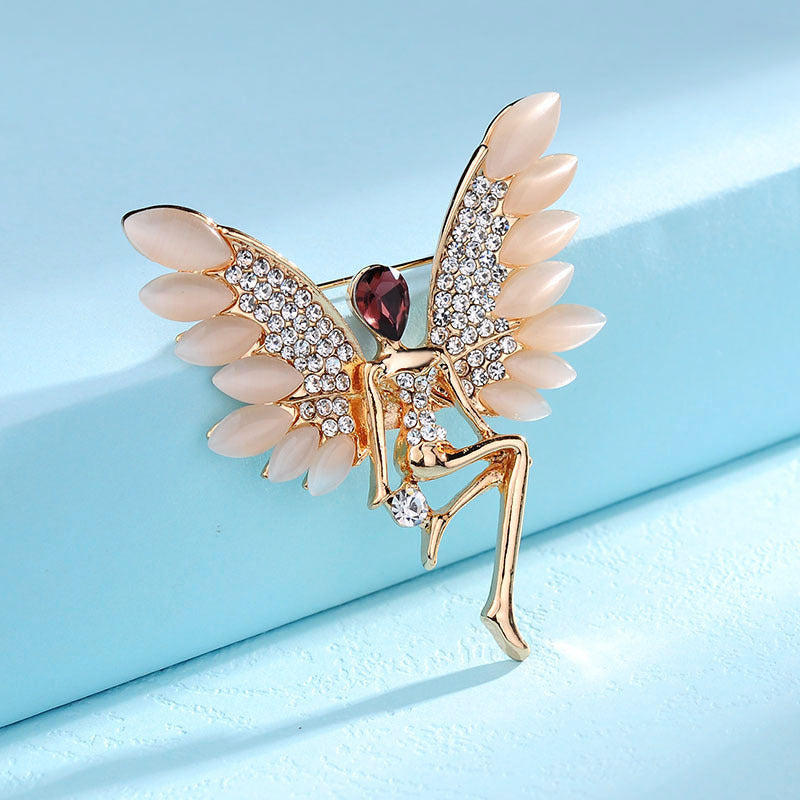 Decorative brooch with angel wings and a red gemstone on a light blue background