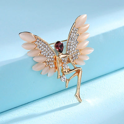 Decorative brooch with angel wings and a red gemstone on a light blue background