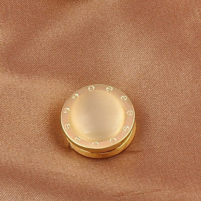 Gold mechanical brooch with a beige center on a brown fabric background