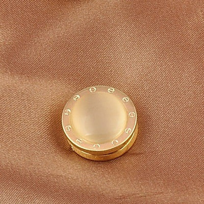 Gold mechanical brooch with a beige center on a brown fabric background
