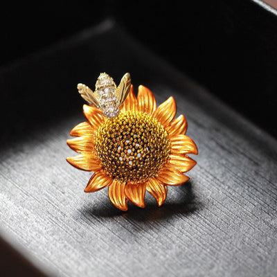 Sunflower-shaped brooch with a bee on a dark surface