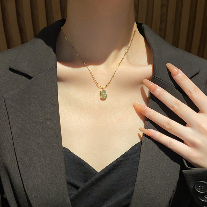 Person wearing a gold necklace with a green pendant, touching their chest.