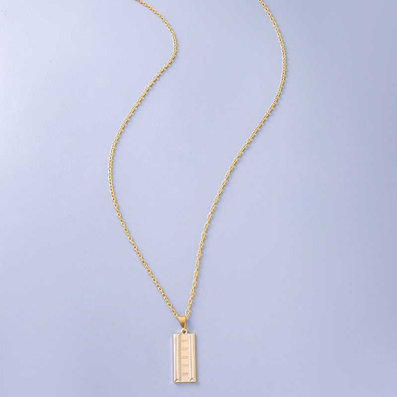 Gold necklace with a rectangular pendant on a light purple background