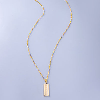 Gold necklace with a rectangular pendant on a light purple background