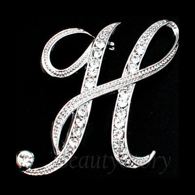 Silver letter 'H' brooch with rhinestones on a black background